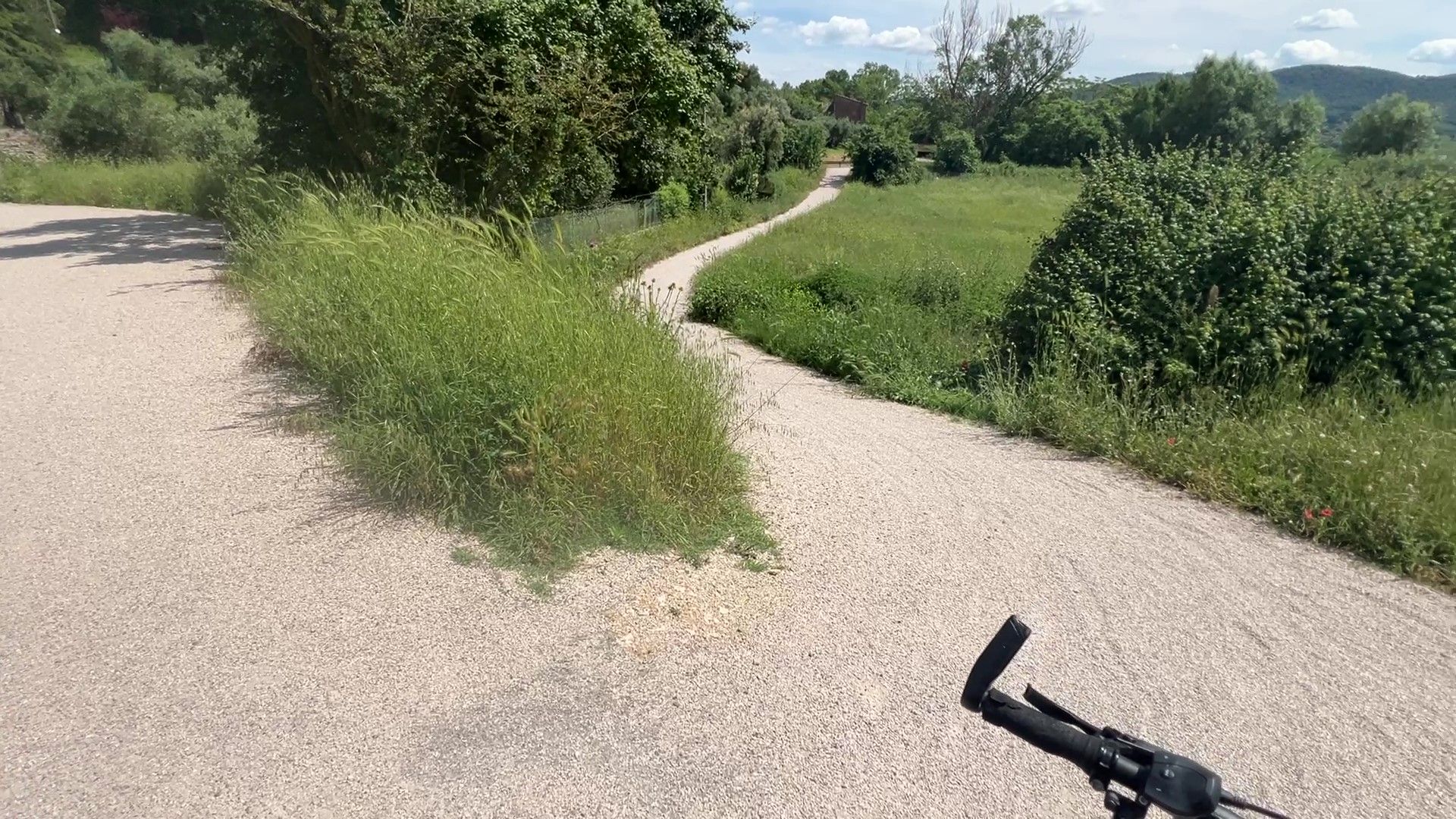 Scharfe und steile Kurve auf dem Radweg. Schotterweg zwischen Bäumen und Feldern.